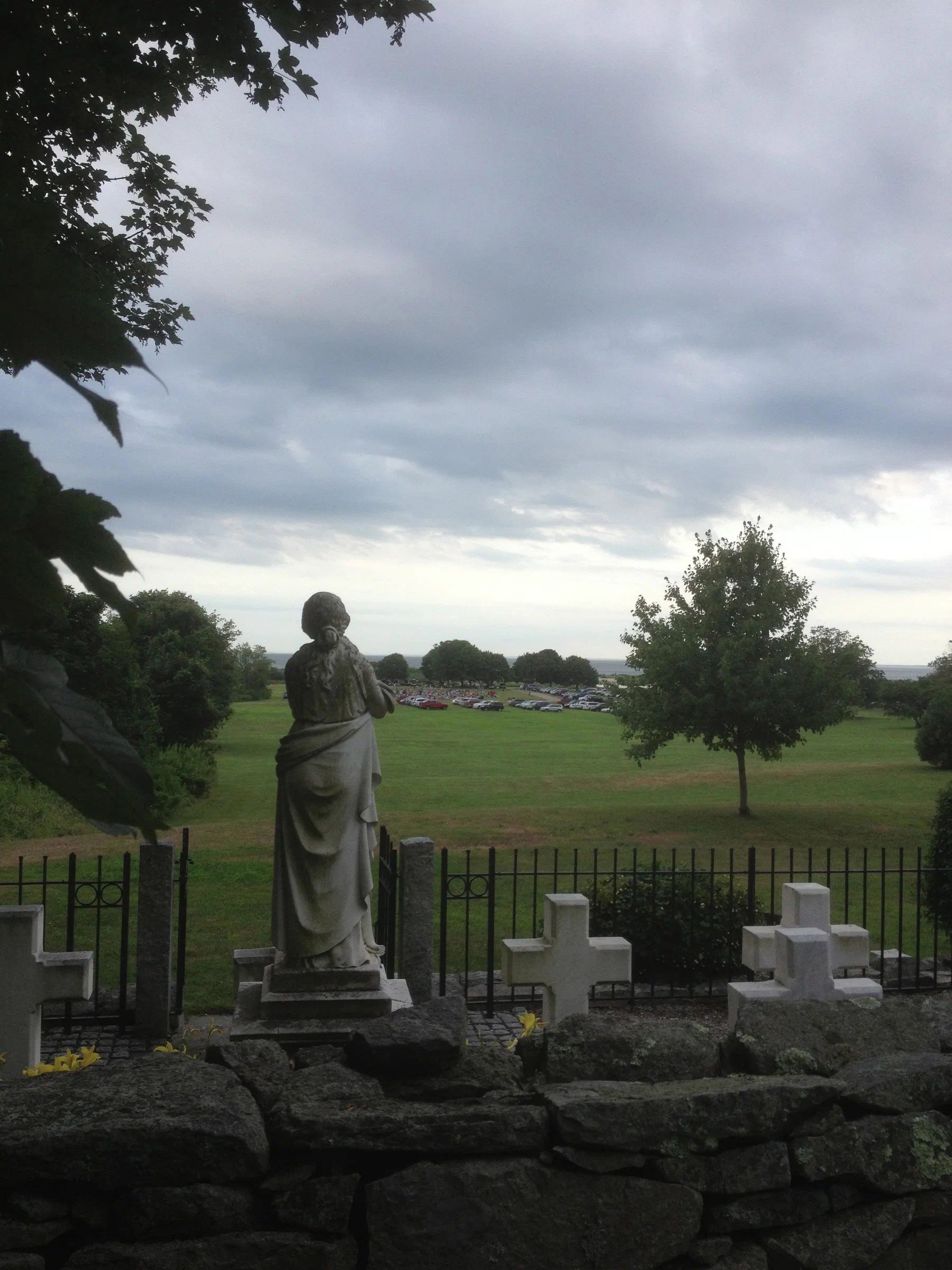 A statue overlooks the grounds and shoreline at the Eugene O'Neill Theater Center beneath a cloudy sky.