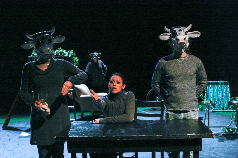 Three performers gather around a table while two wear animal masks.