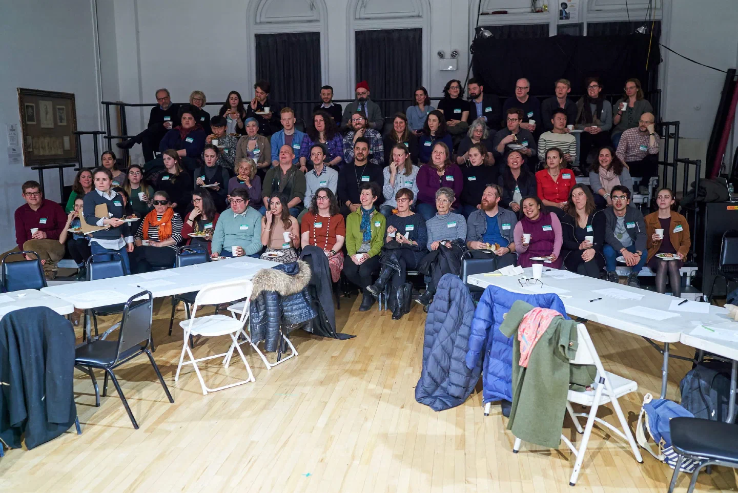 A large group poses together behind tables in a community hall.