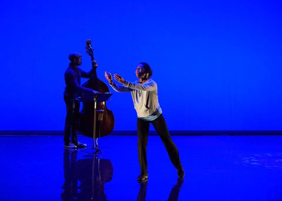 Two performers reach toward each other against a vivid blue background.