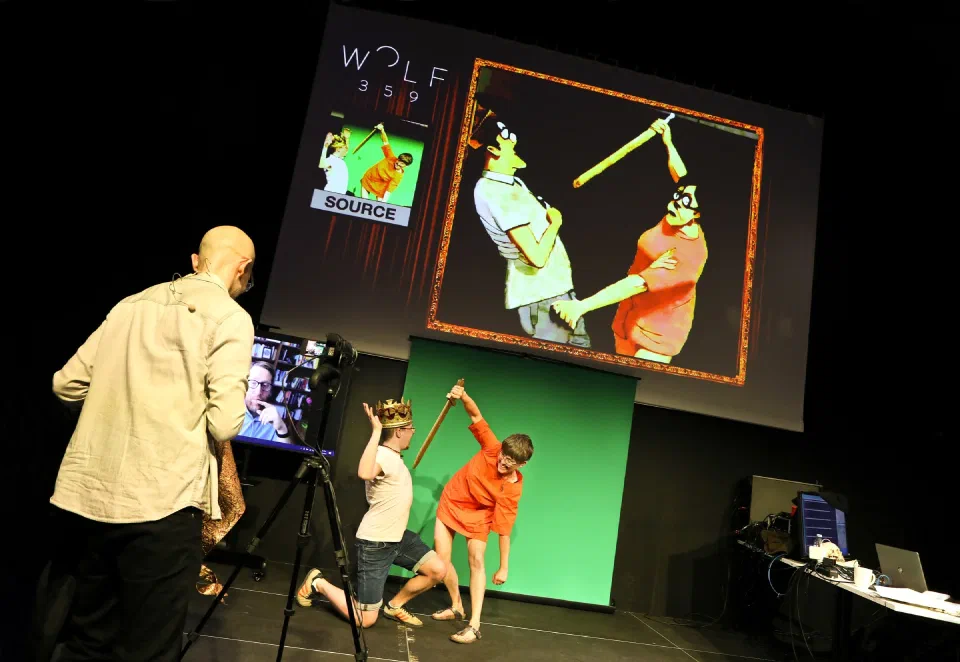 Performers enact a scene before a projection showing a live source view and a generated image.