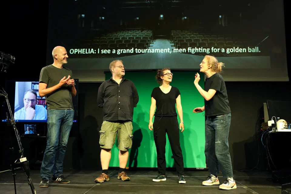 Four performers rehearse beneath a projected line of dialogue generated for Ophelia.