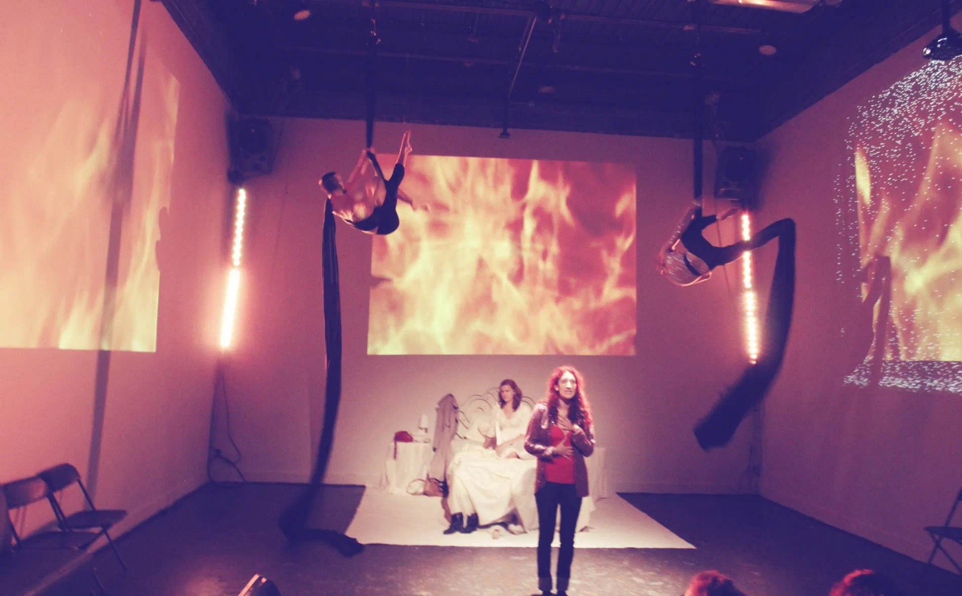Two women perform below aerial figures and projections of flames and textured imagery.