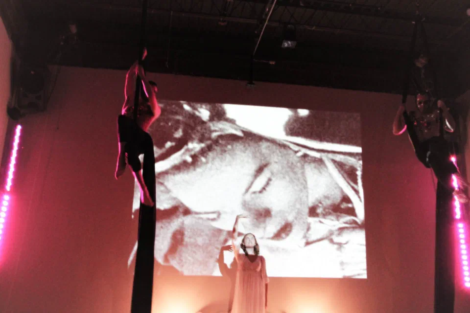 A suspended performer hangs above a stage filled with projected imagery.