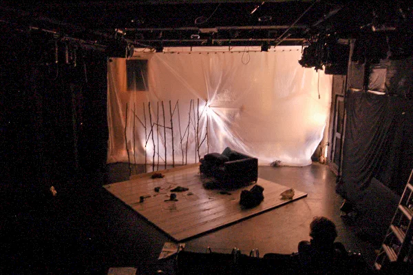 A grand piano sits on a mostly empty stage before a translucent white backdrop.