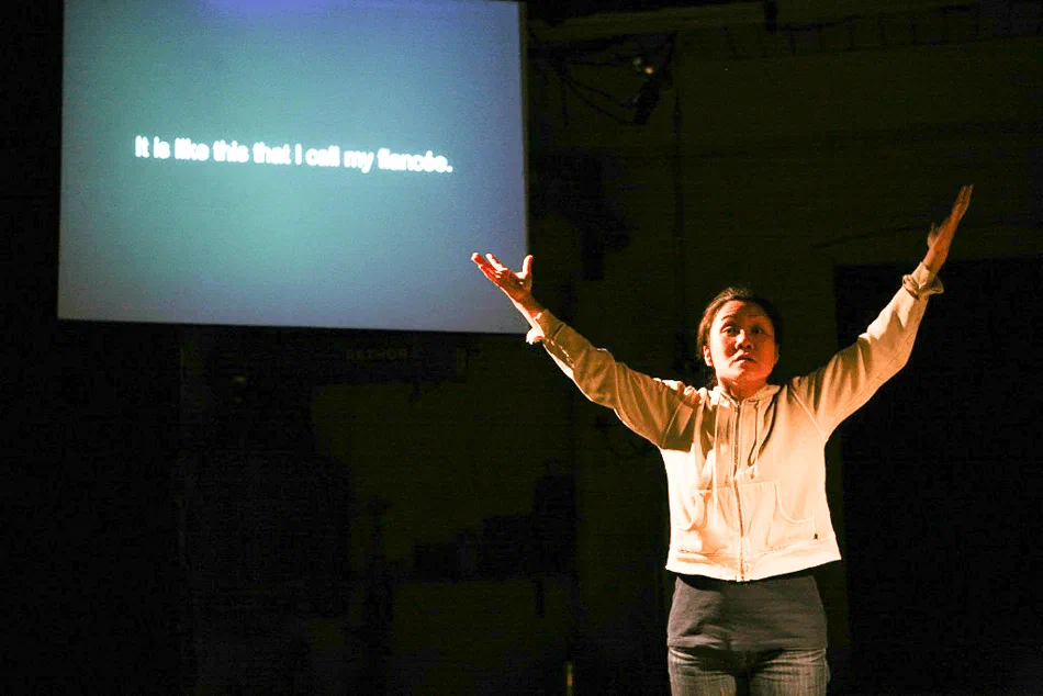 A woman raises both arms beneath a screen displaying projected text.