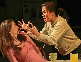 Two performers confront each other across a table during an intense scene.