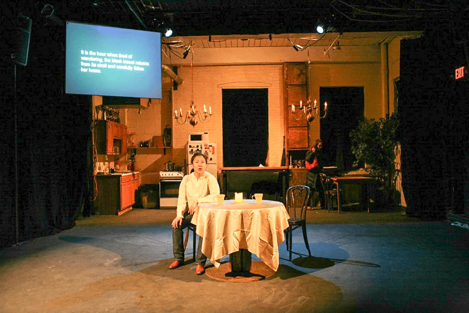 A woman sits alone at a round table within a detailed domestic set.