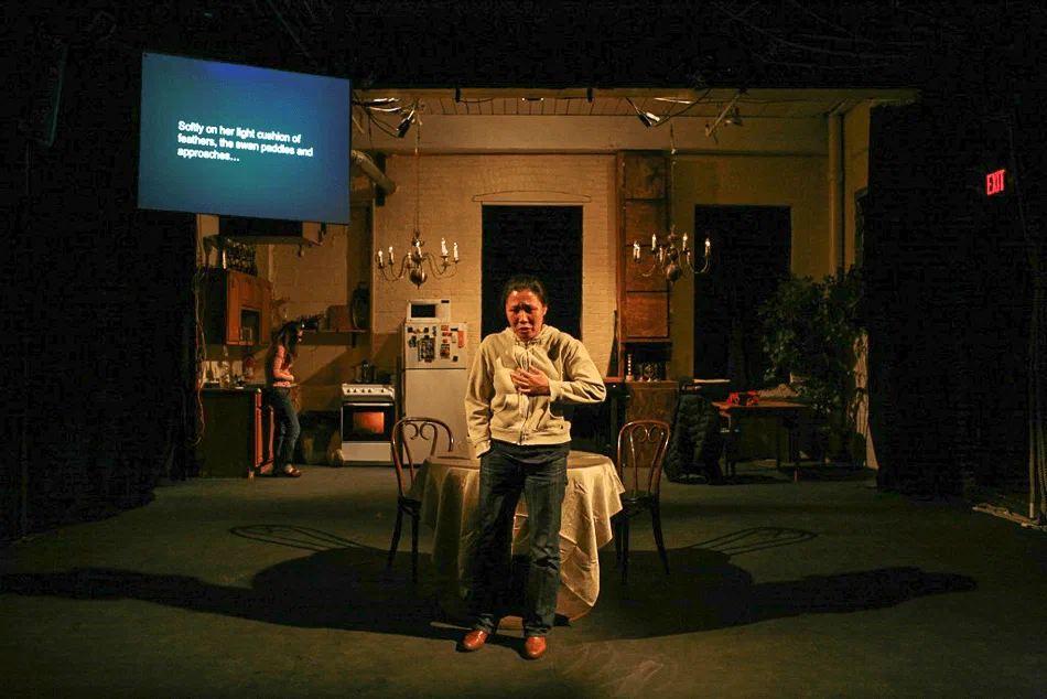 A woman addresses the audience beside a round table beneath a projection screen.