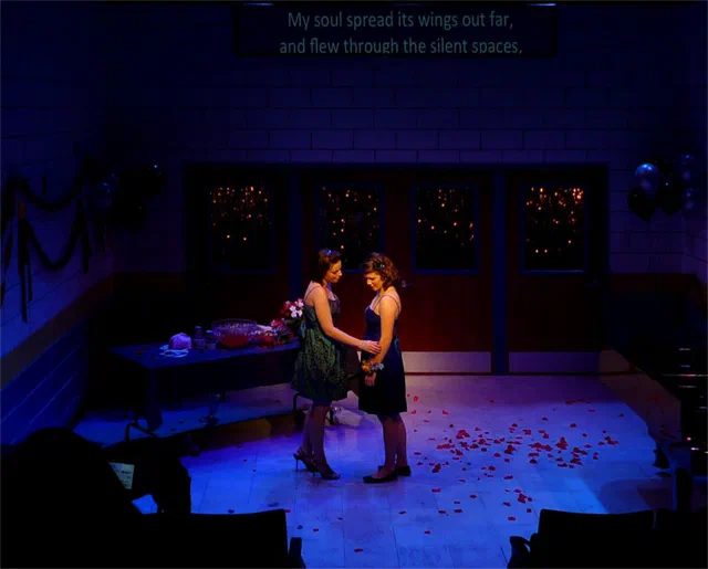 Two performers face each other beneath projected text on a festive set.
