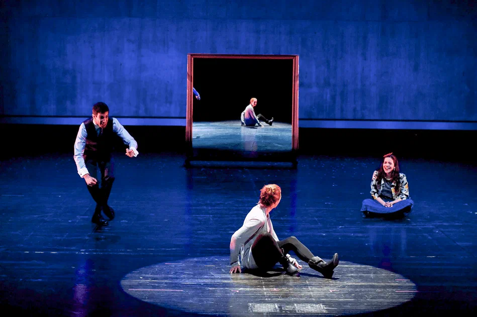 Performers occupy a blue stage arranged with glowing rectangular frames.