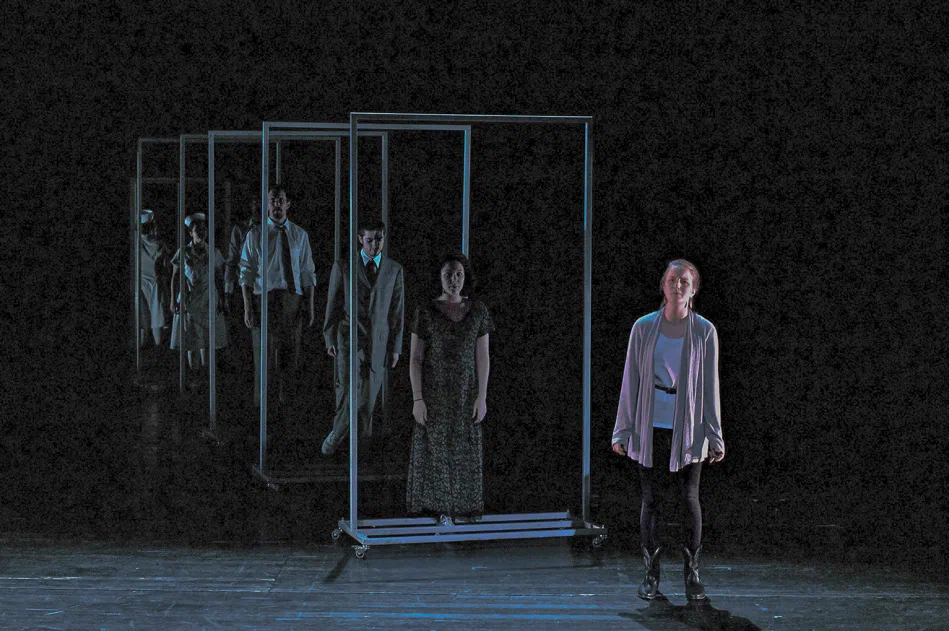 A woman stands before a rectangular frame containing several shadowed figures.