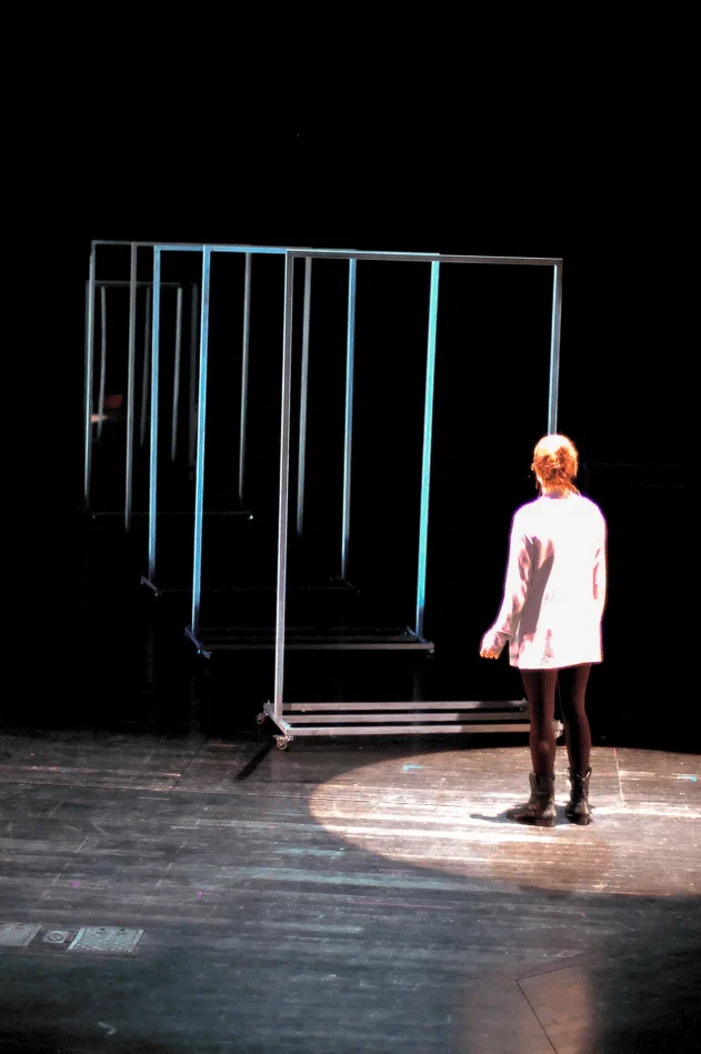 A lone performer faces a row of tall illuminated frames on a dark stage.