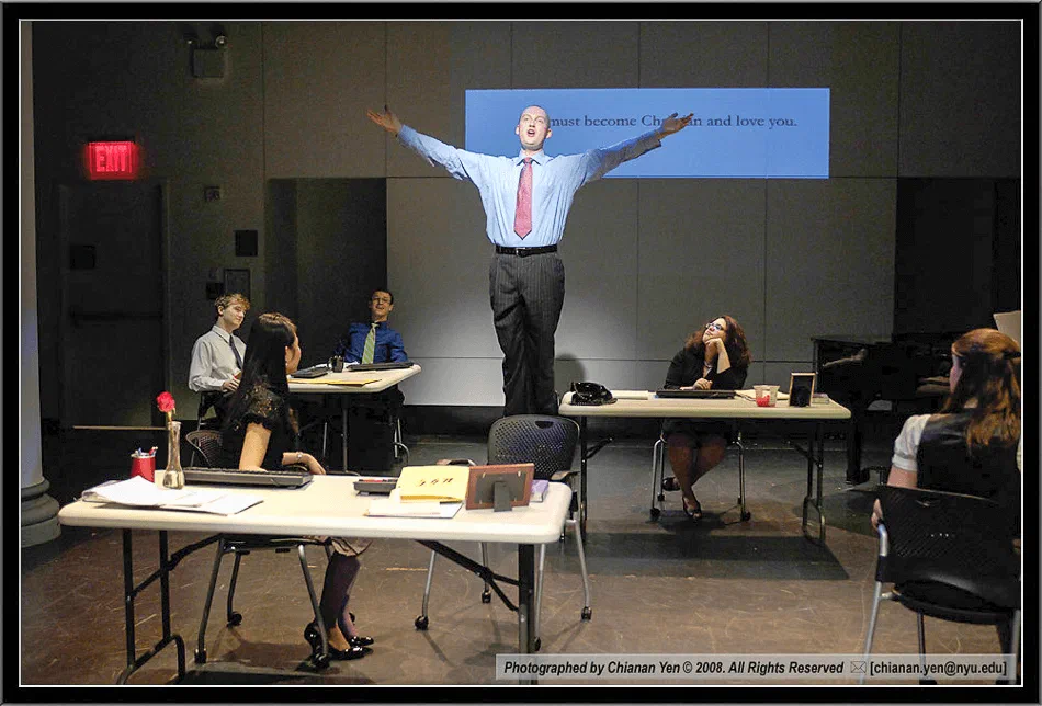 A performer throws his arms wide above tables arranged across the stage.