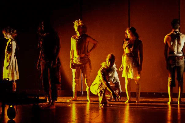 An ensemble stands in a line under saturated amber stage light.