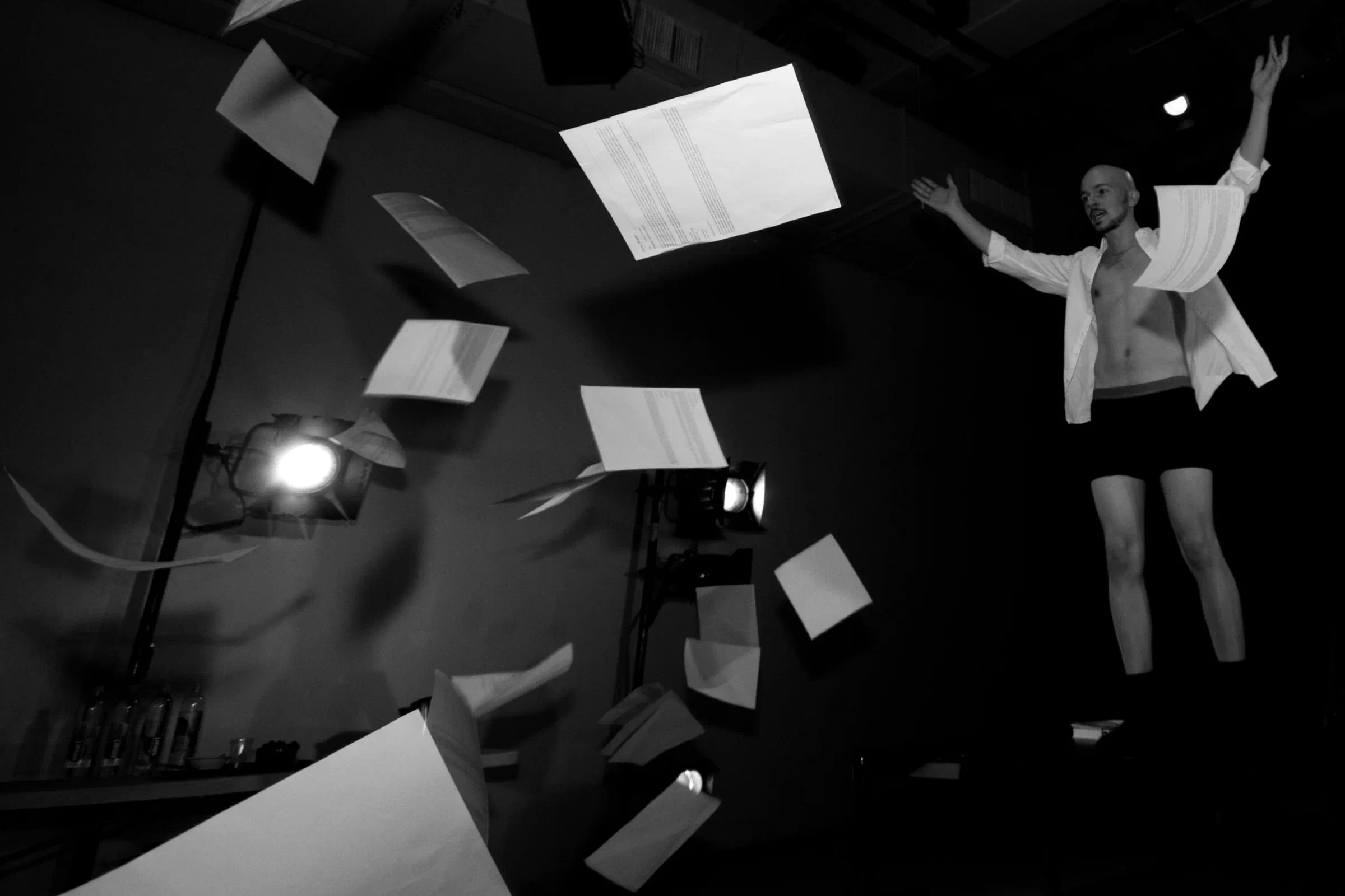 Loose papers fly around a performer suspended above a black-and-white stage.