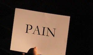 A hand holds a white card printed with the word PAIN.