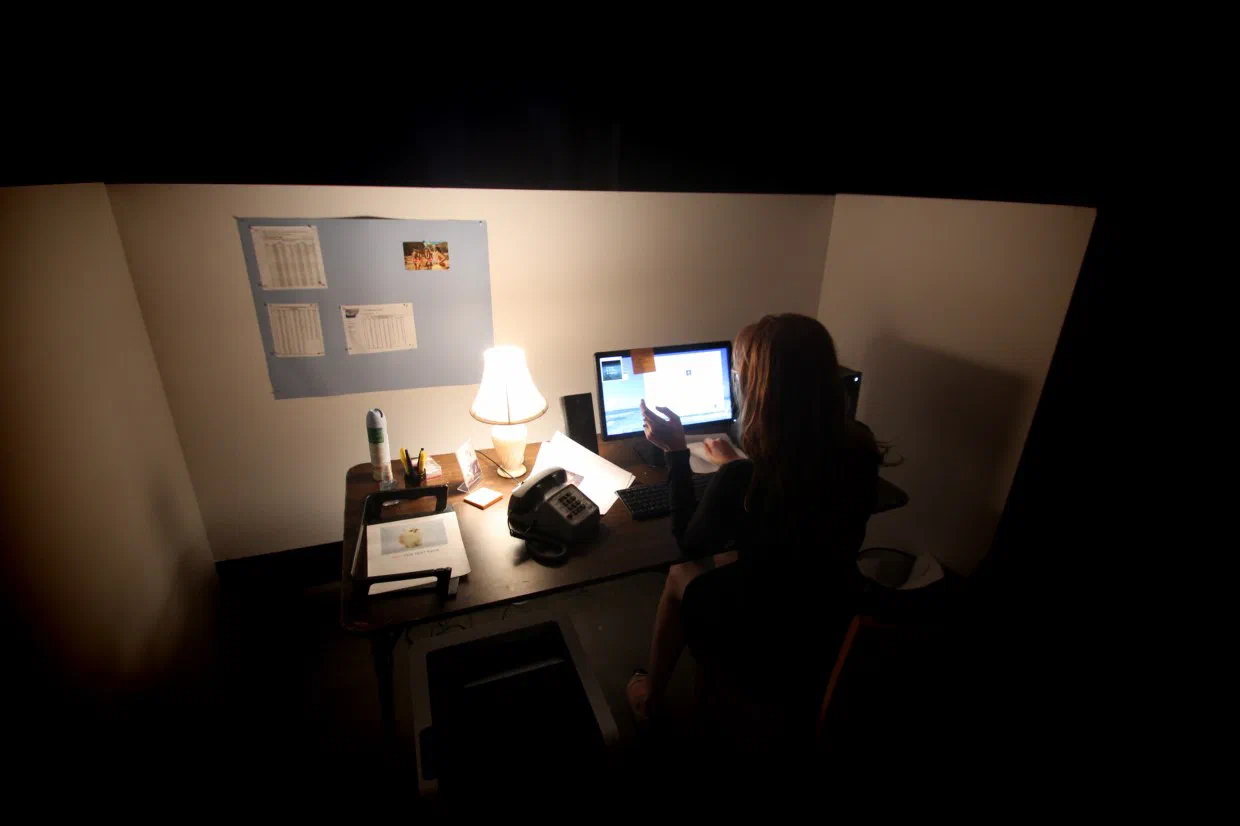 An audience member sits alone at the illuminated Temping desk in a dark room.