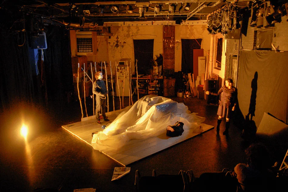 A billowing white sheet stretches across a stage lit in amber.