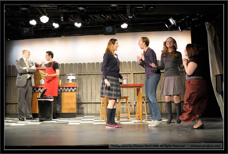 Six performers confront one another across a brightly lit cafe set.