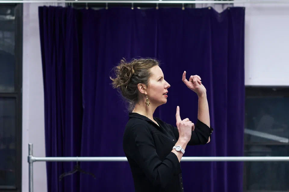 A woman gestures with both hands during a rehearsal in a studio.
