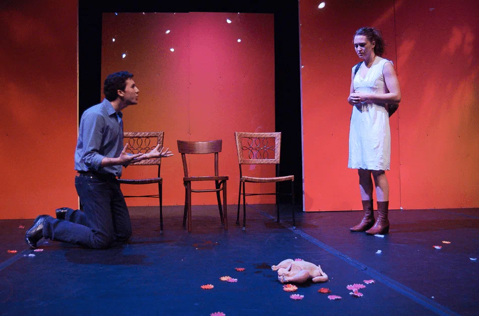 A kneeling man reaches toward a woman in white on a stage scattered with flowers.