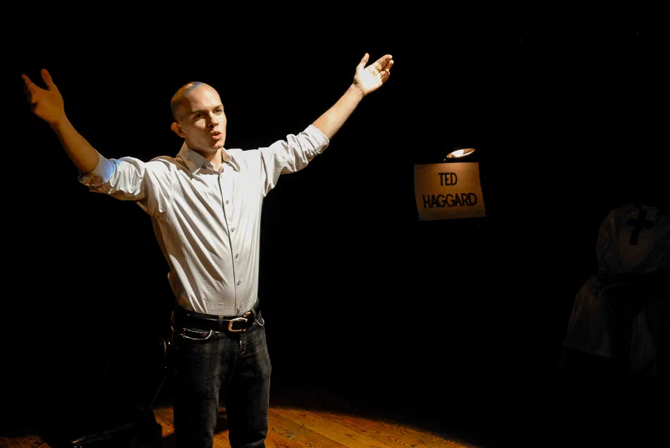 A performer spreads his arms beside a lit Ted Haggard sign.