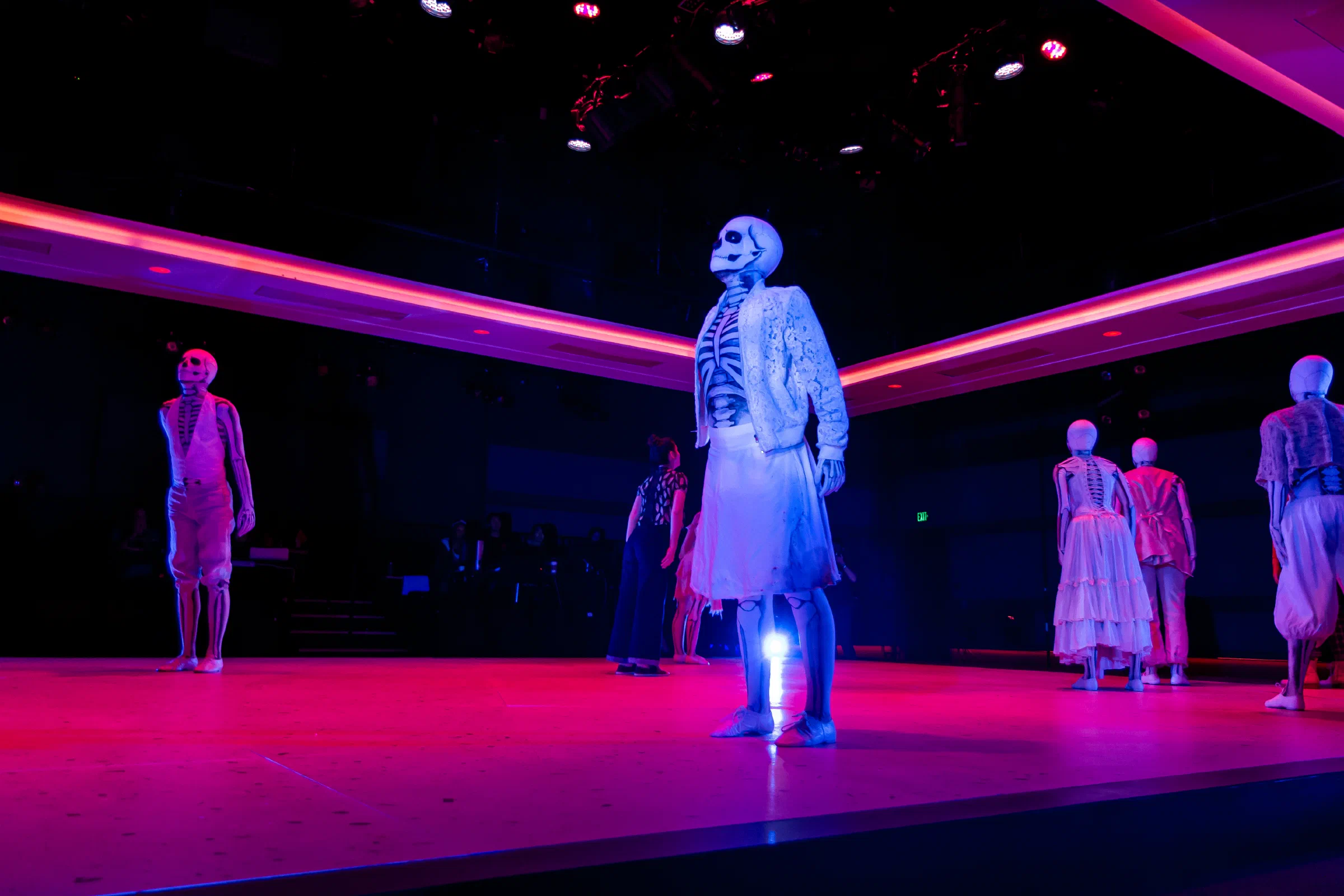 A performer in a skeletal costume stands at the center of a red-and-blue stage.