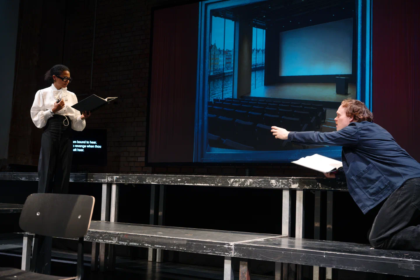 A woman reads from pages as a man reaches across a table toward her.