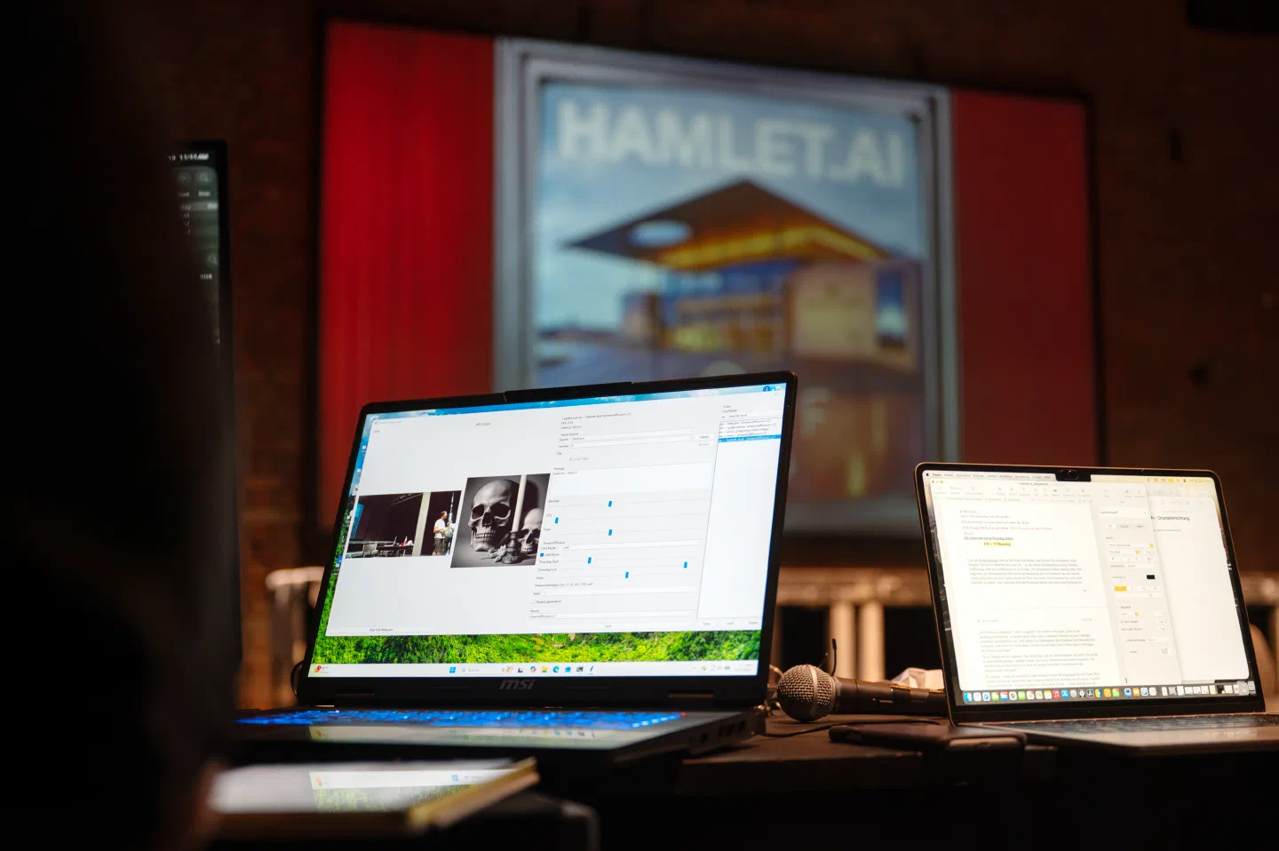 Two open laptops sit in the foreground beneath a projected Hamlet.ai image.