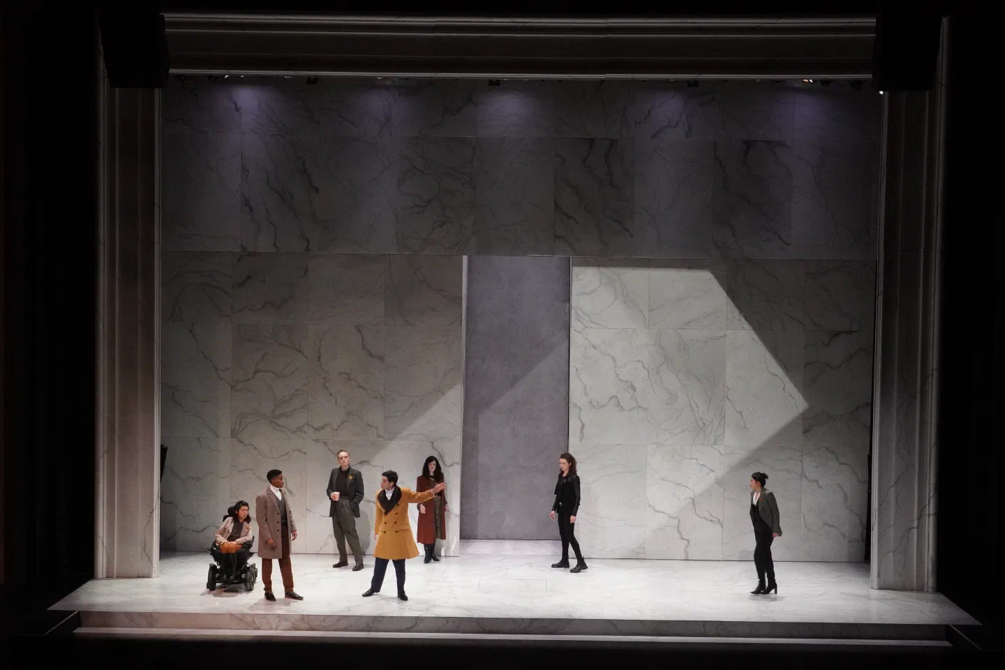 An ensemble stands widely spaced across a monumental pale architectural set.