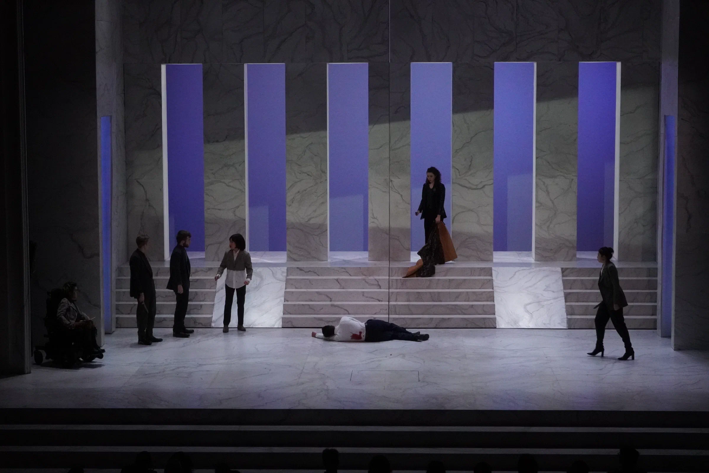 An ensemble crosses a pale architectural set of stairs and tall openings.