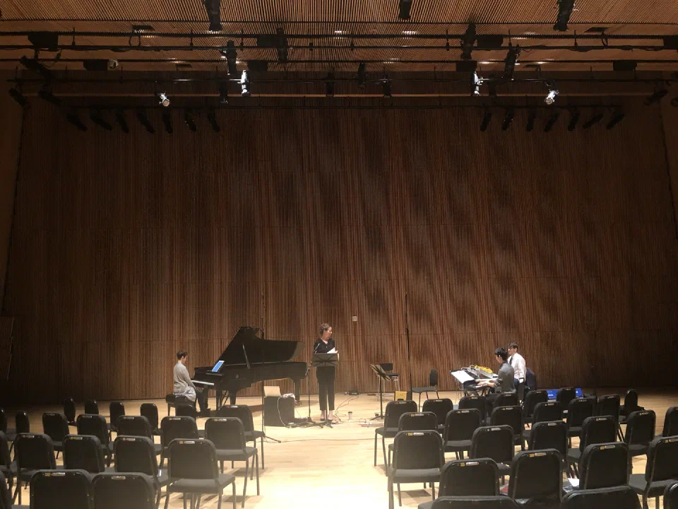 Musicians perform on a wood-paneled concert stage viewed from the audience.