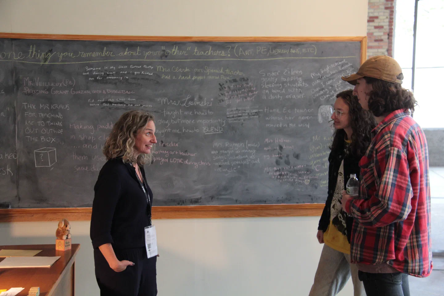 Three visitors talk in front of a chalkboard filled with handwritten memories.