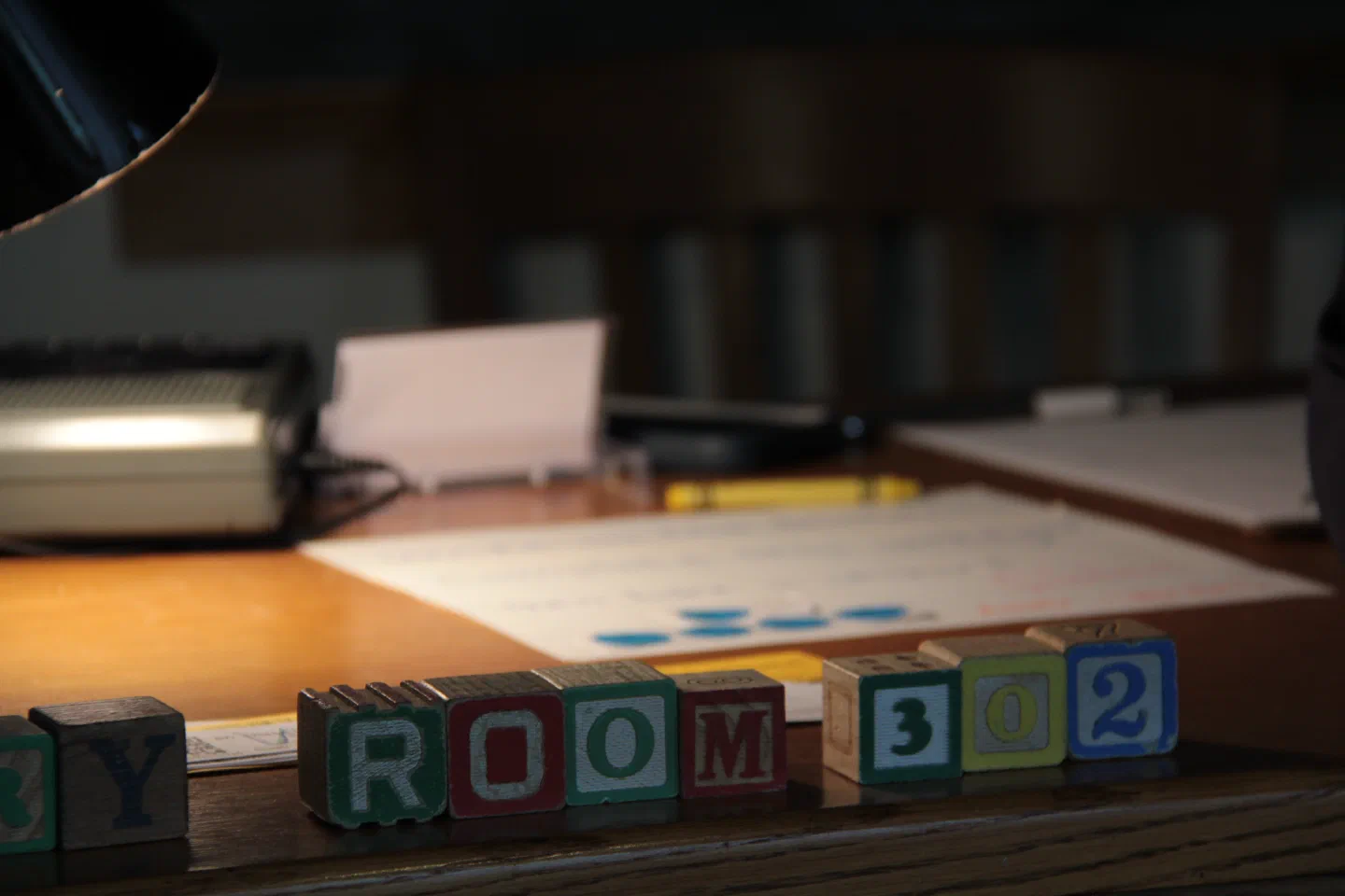 Letter blocks spelling ROOM 302 sit among papers on a lamp-lit desk.