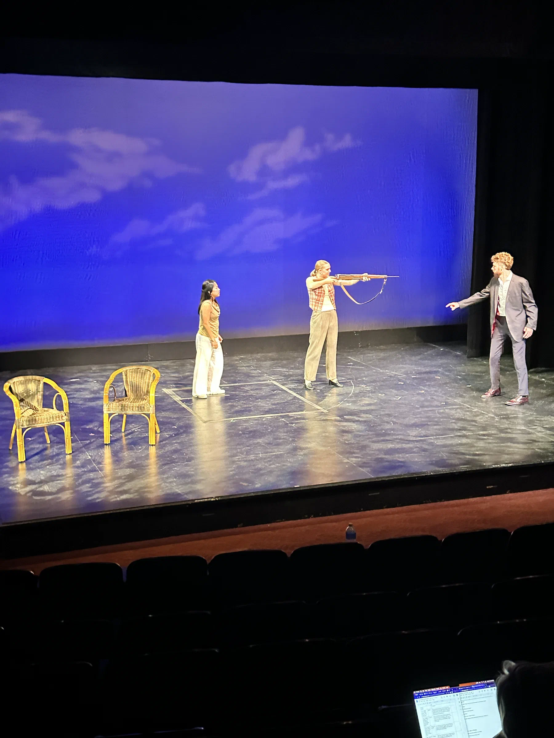Four performers stand across a blue stage beneath a projected field of clouds.