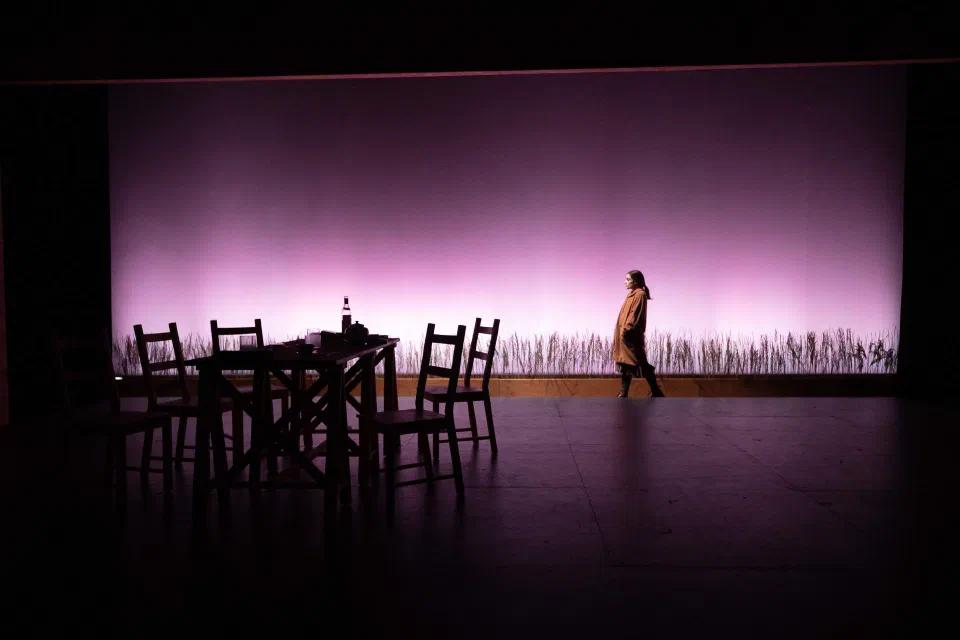 A lone performer crosses a stage fading from black into lavender light.