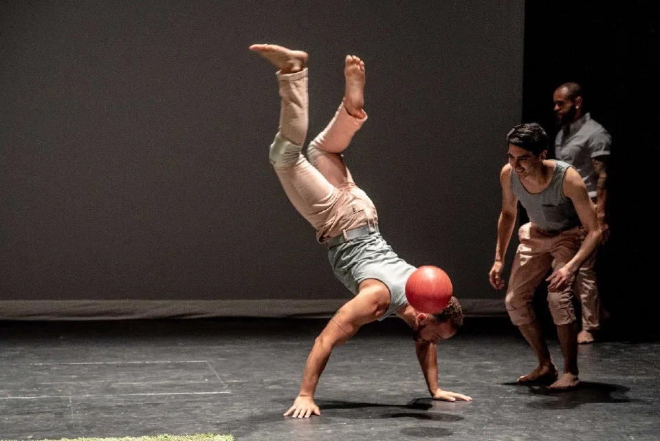 A performer balances upside down on one hand as the ensemble watches.