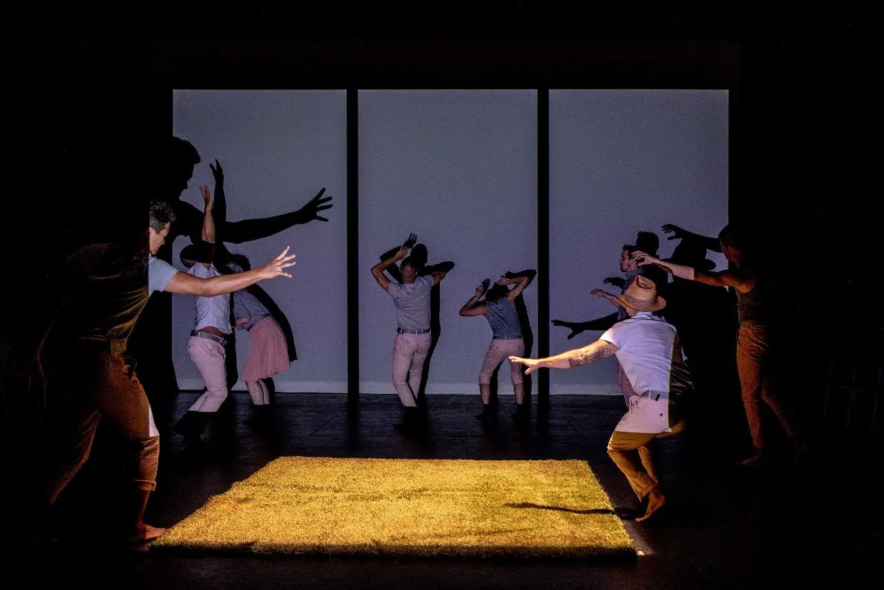 Performers reach around tall translucent panels bordering a yellow floor.