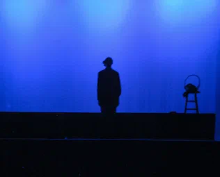 A lone silhouetted figure stands on a raised platform against a blue background.